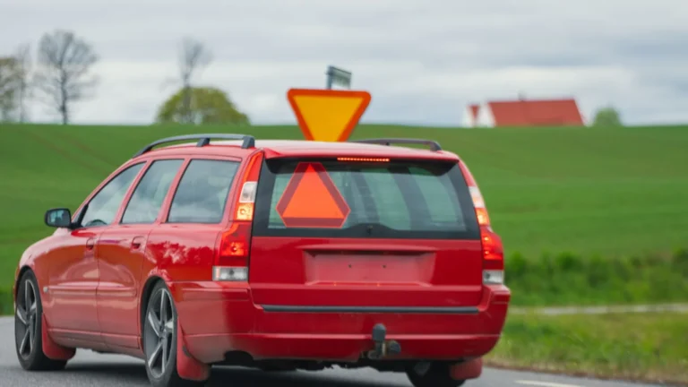 A red car drives on a countryside road in Jönköping, Sweden with a rural landscape — SSK Mechanics guide to Halfords Summer Car Check vs SSK Mechanics: What Each…