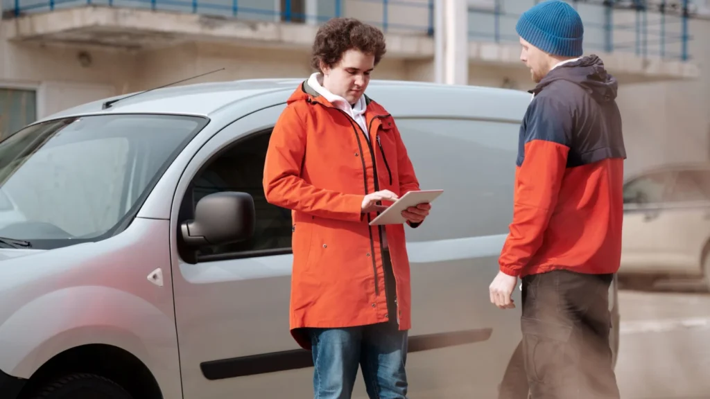 Two delivery men in bright jackets using a digital tablet beside a van outdoors — SSK Mechanics guide to DIY Car Repair vs Booking ClickMechanic or a Local Mobile…
